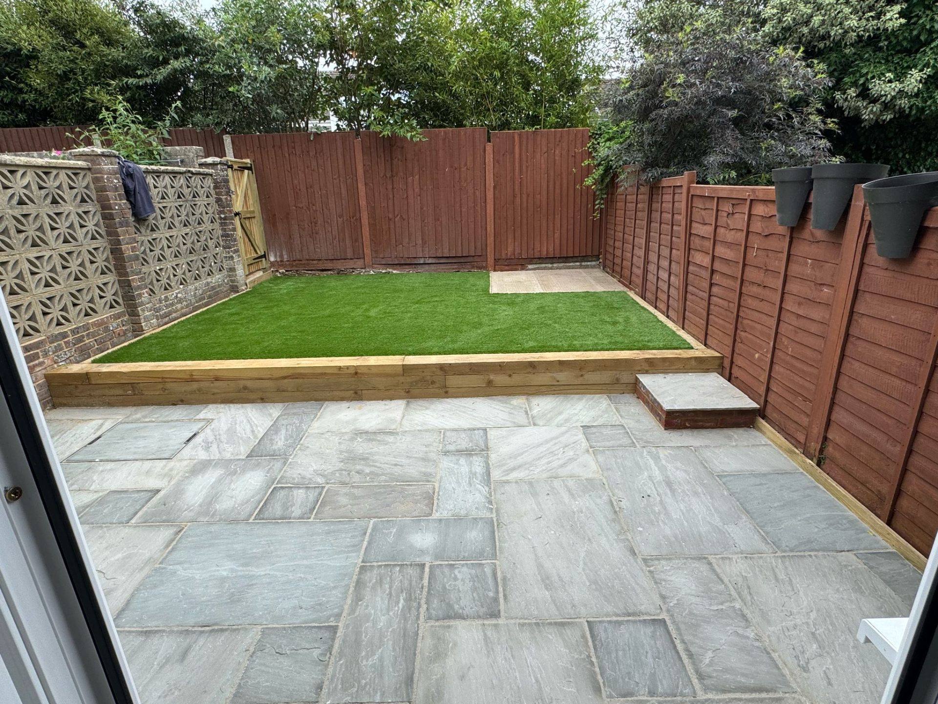 Grey sandstone patio with raised artificial lawn behind sleeper retaining wall by A Baker Construction West Sussex