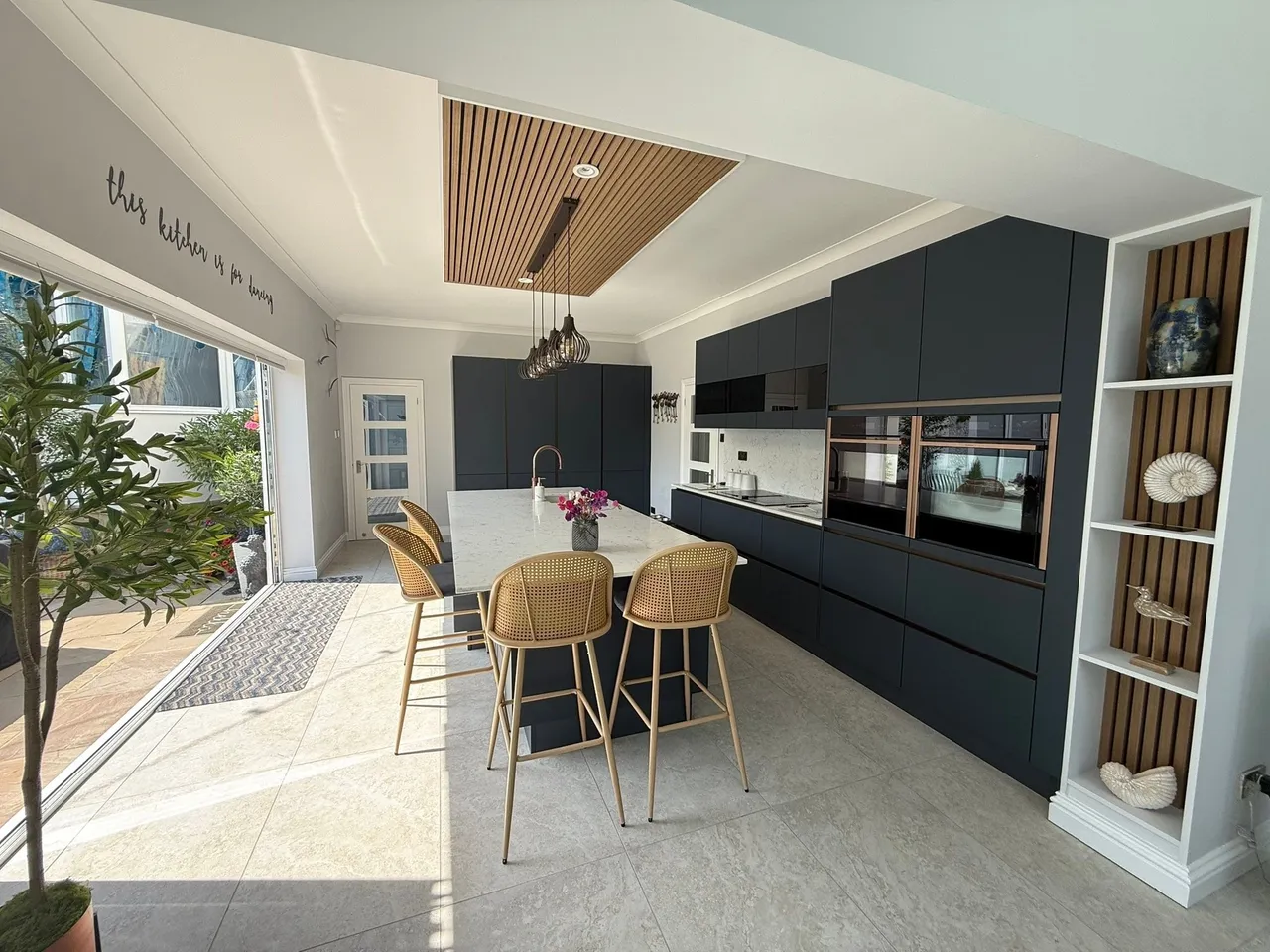 Modern navy handleless kitchen with island, timber slat ceiling and rattan bar stools West Sussex
