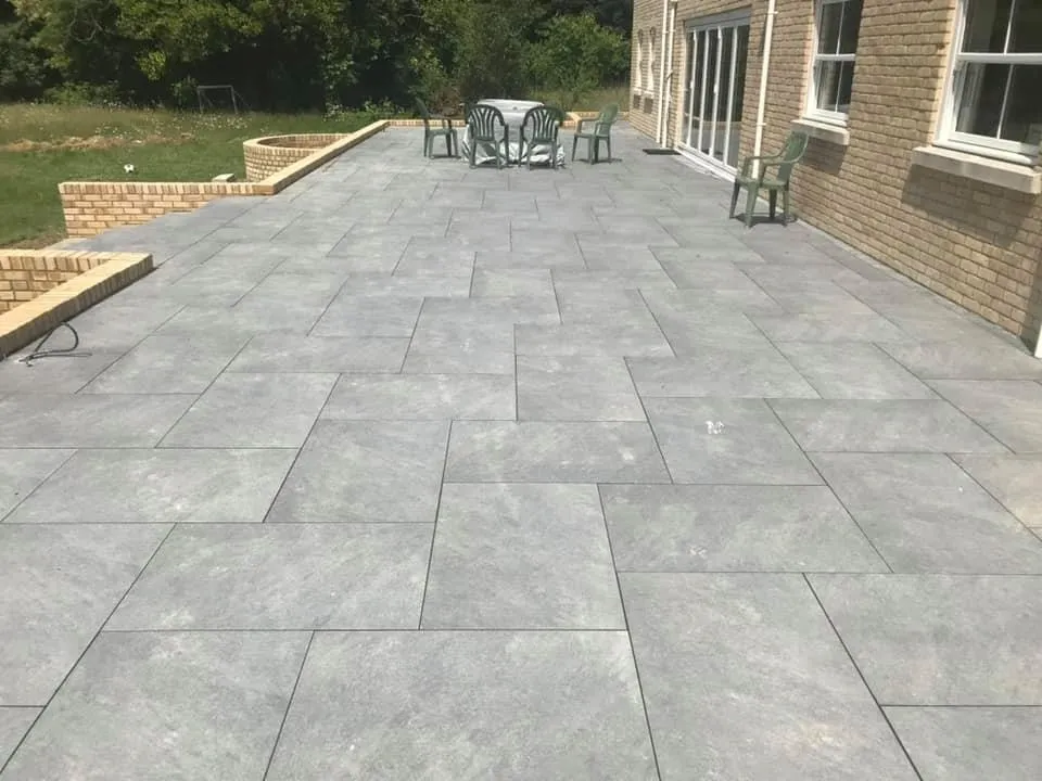 Large grey porcelain patio with raised brick planting beds by A Baker Construction West Sussex
